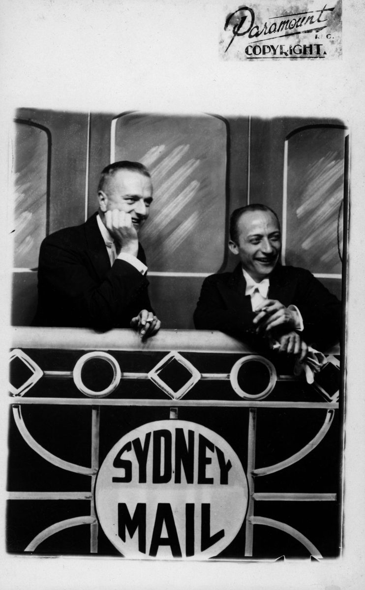 Two gentlemen in dinner suits posing with a backdrop of the 'Sydney Mail train' at the Trocadero, South Brisbane (1938)