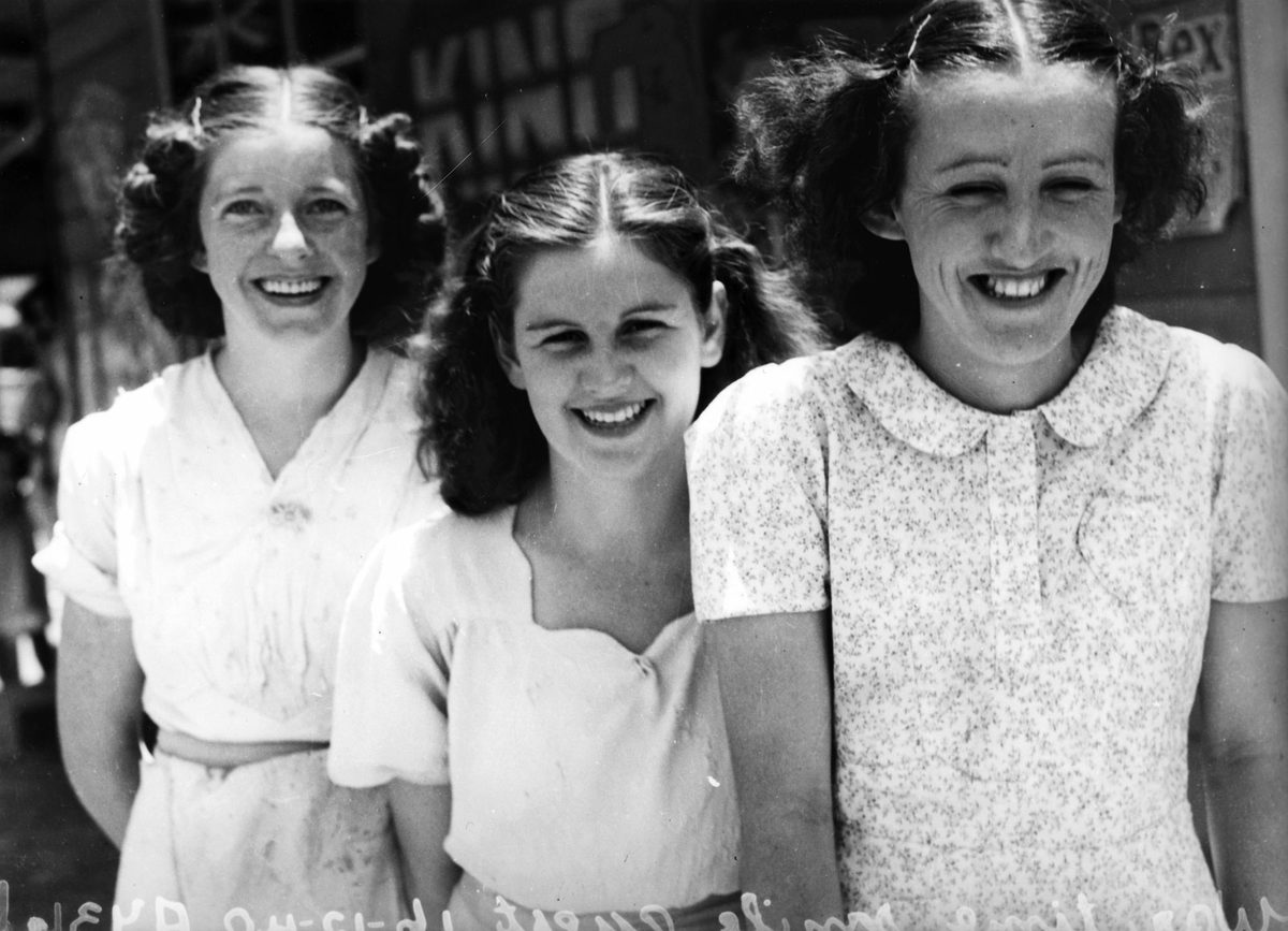 Three girls smile brightly for the Wartime Smile Quest to aid the Patriotic Fund of Queensland, Brisbane, 1940