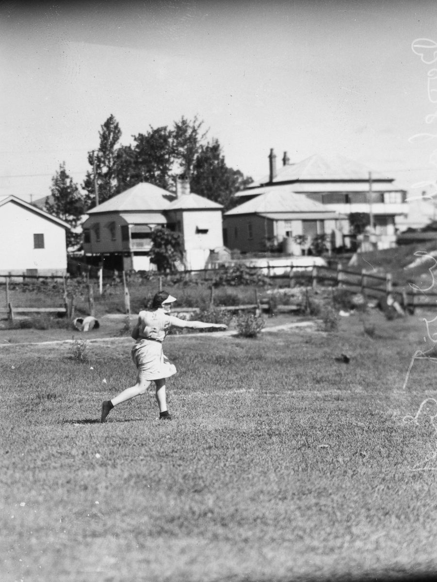 Woman playing baseball behind a row of houses in Brisbane, 1938