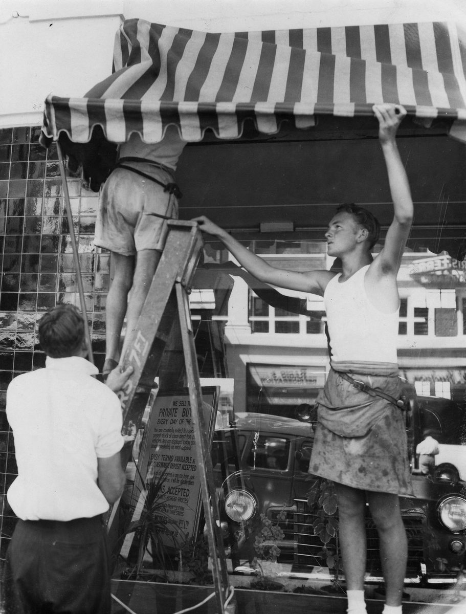 Council workmen pulling down a canvas awning infront of Christeys Motors, Adelaide Street, Brisbane, 1953, Brisbane City