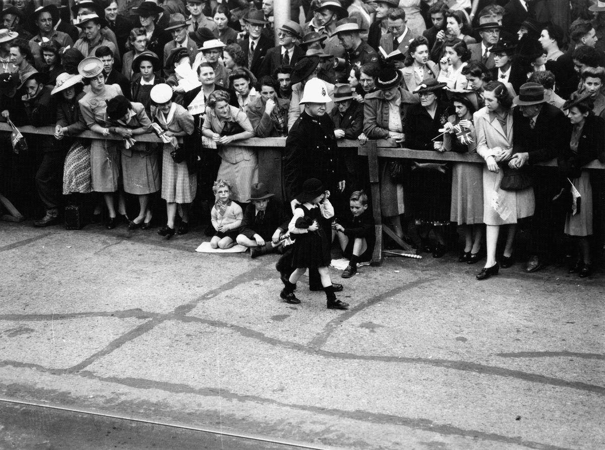 Policeman assists a small girl who is part of the crowd waiting to see the military procession, Brisbane August 1940 (1944)