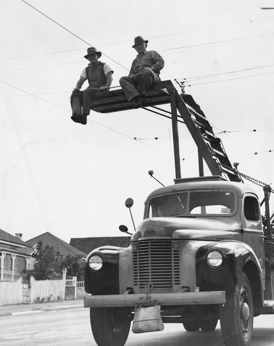 Tramway workmen sitting on an elevated platform under overhead tram lines, Brisbane, 1949