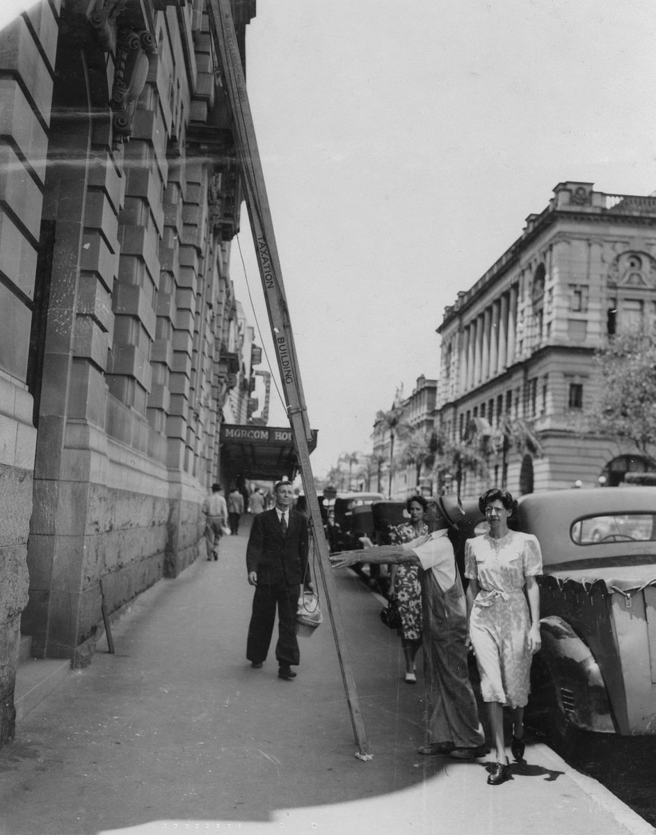Workman supporting a ladder on George Street, Brisbane, 1949, Brisbane City